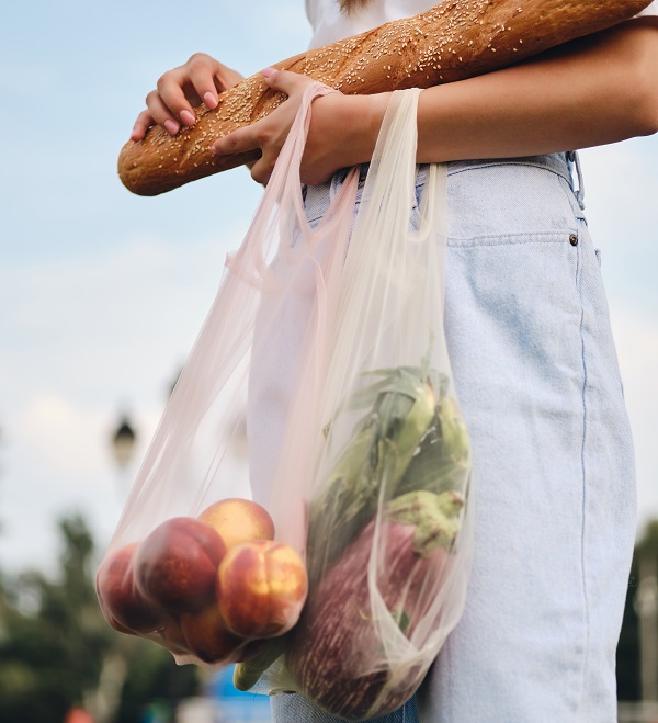 Close up woman standing with baguette bread,peaches and vegetables in eco bags in city park